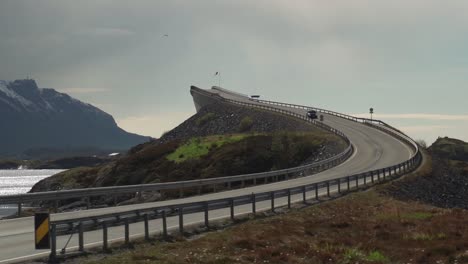 a view of the famous atlantic road in norway. one of its'  arched bridges rises above the sea. it is overcast, with heavy clouds hanging above the water.
