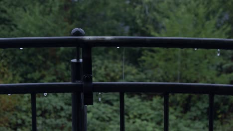 Balcony-view-of-a-rainy-day-outside,-rain-drops-are-falling-down-from-black-colored-metal-outside-fence,-everyday-life-concept