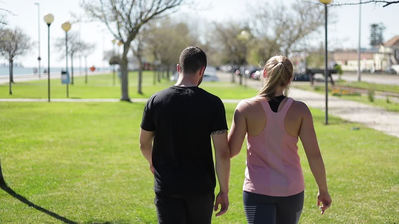 vista trasera de una joven pareja deportiva caminando por el césped verde en el parque.