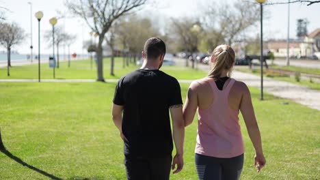 back view of sporty young couple walking on green grass in park.