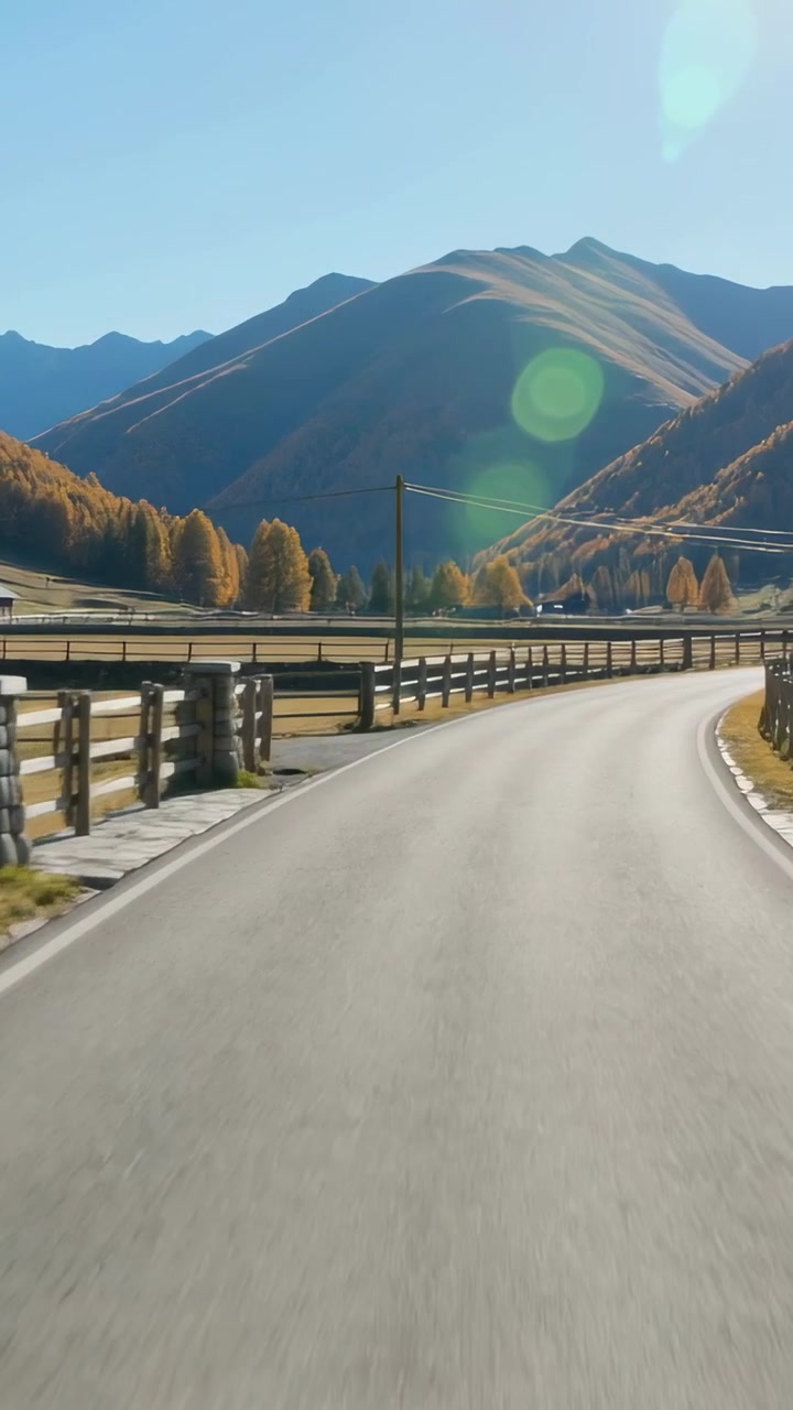 Video verticale: Veicolo che parte, telecamera che riprende una strada asfaltata verso la base della montagna, recinzioni di legno.