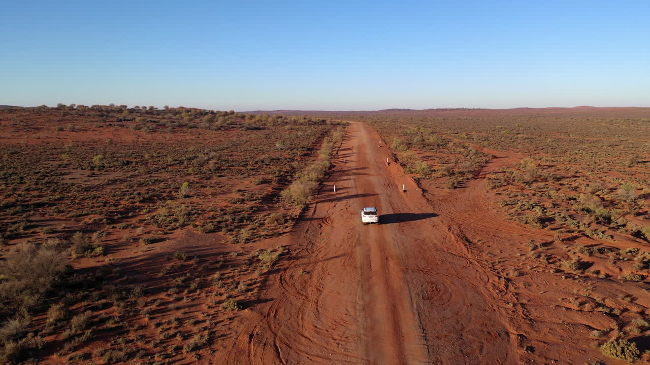 antena: disparo de un dron siguiendo de cerca a un vehículo blanco mientras conduce por una polvorienta carretera roja del interior, cerca de broken hill, australia