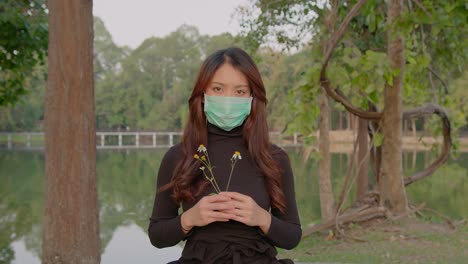 woman wearing mask in a park holding flowers