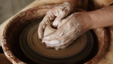 close-up of potter's hands with red manicure working with wet clay on a pottery wheel making a clay product in a workshop. unrecognizable female person. slow motion