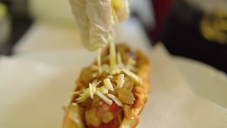 Geriebenen-Käse-Auf-Frisch-Gegrillten-Hotdog-Geben