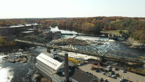 Aerial-view-old-mill-building-beside-a-bridge-crossing-river-with-dam