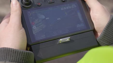 a worker in a yellow hi-vis vest at a construction site operating a drone