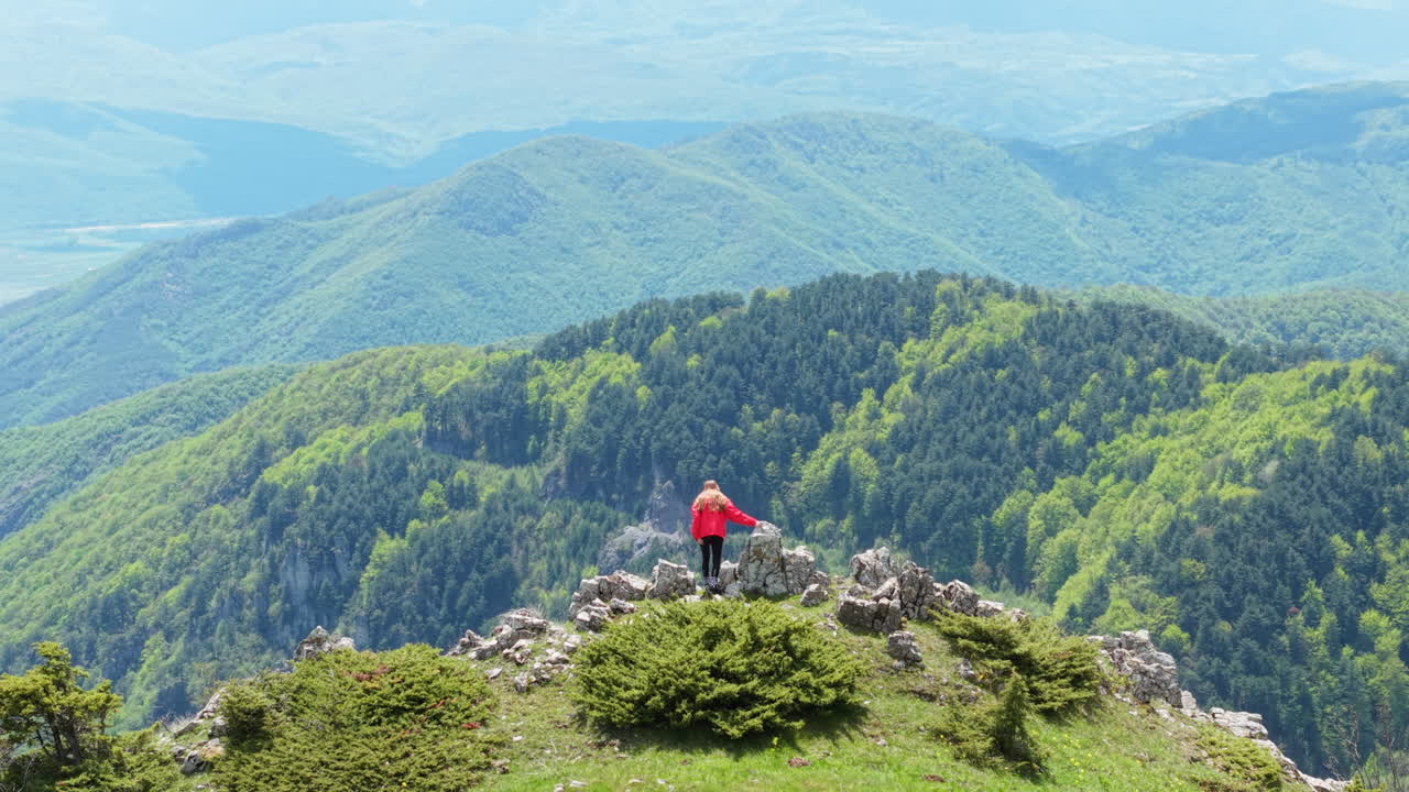 A young woman hiker pauses on a high cliff in the Bulgarian mountains, surrounded by green wilderness and clear skies. The image captures freedom, travel, and the joy of spring exploration.