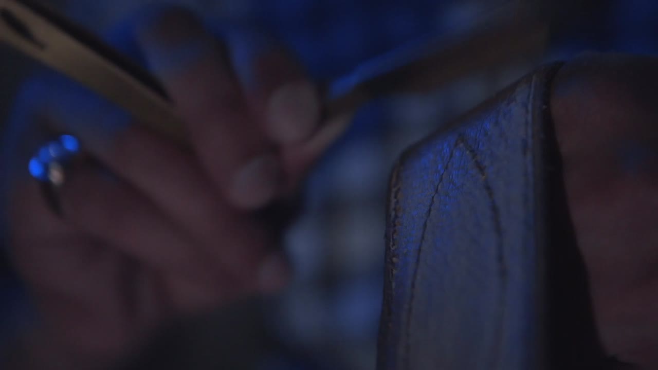 vista de cerca de una persona que trabaja con una navaja y las manos, trabajando en una pieza de madera y cuero, en una habitación oscura.