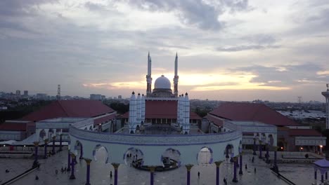 reveal drone shot of the great mosque of central java (majt) in suset time. th sun is orange and the weather is cloudy. it have some pillars and some umbrela that is closed