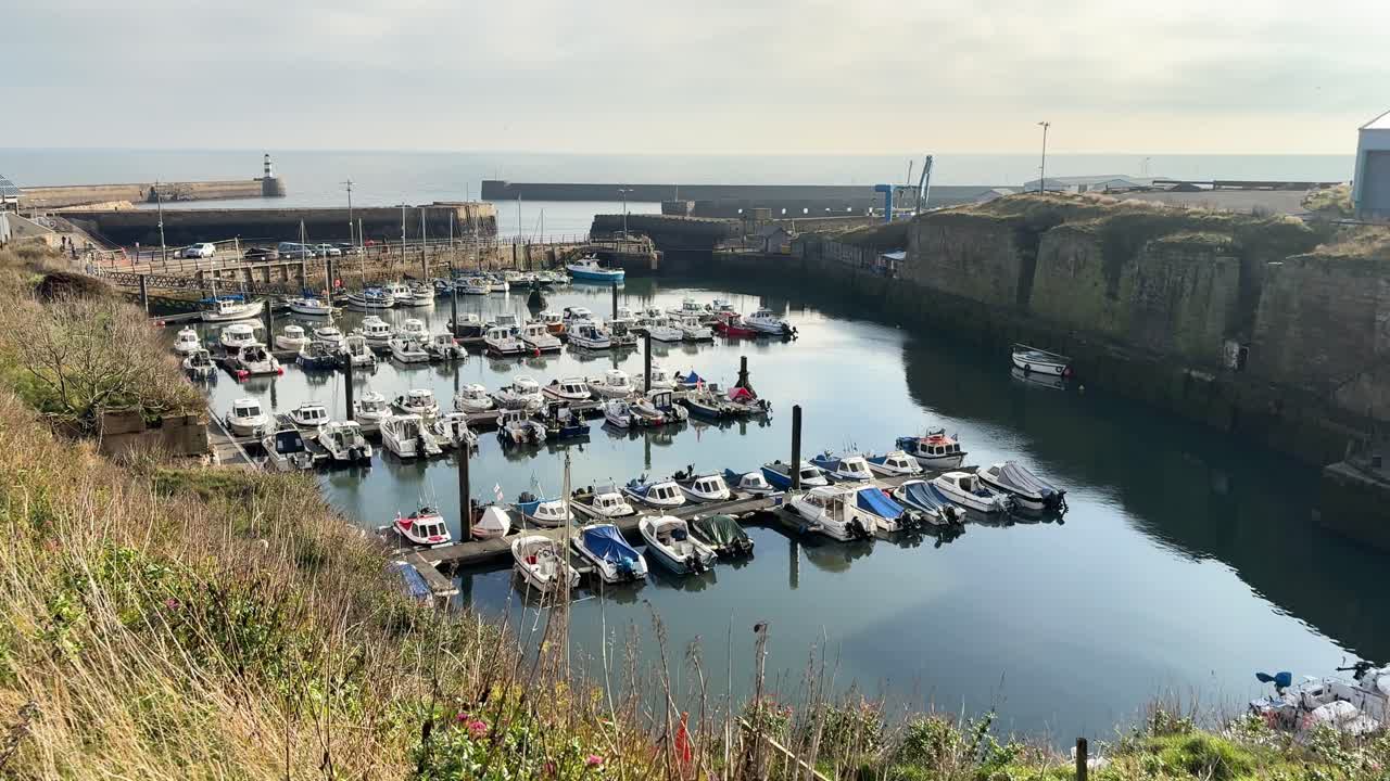 Small boats moored in harbour with lighthouse in distance. Seaham - County Durham, UK