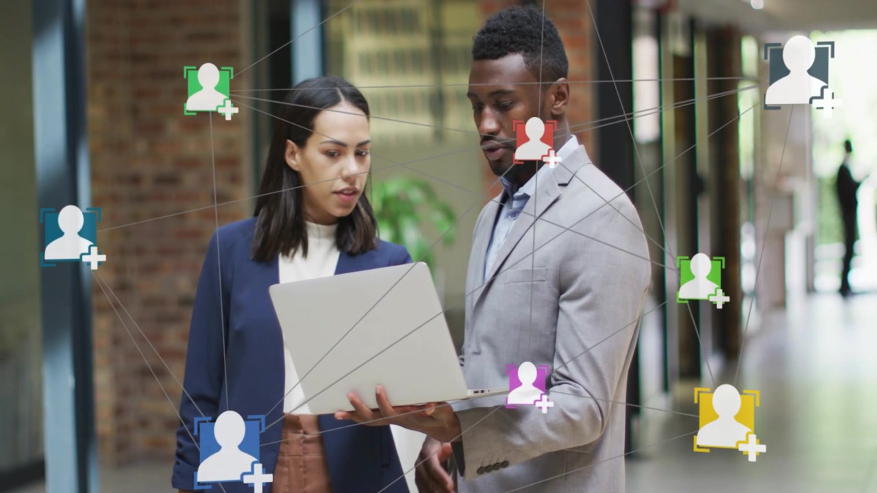 Man opening laptop and woman flipping binder in hall comparing business data while icons overlaying