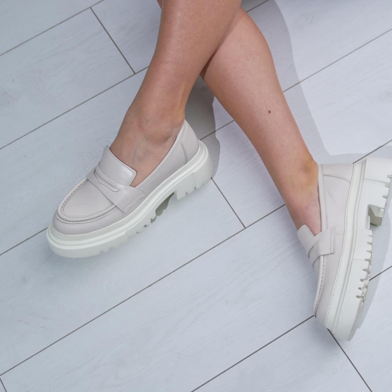 Bare legs of a female model wearing white shoes on tractor soles. Woman changes her position to demonstrate stylish footwear