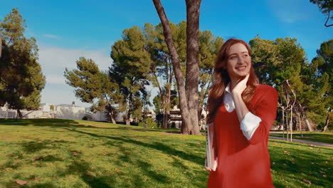 a happy, attractive, young, caucasian woman at the park, walking and smiling while carrying her laptop under her arm