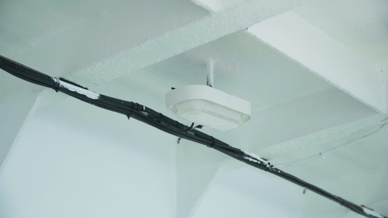 Primo piano di un sistema di rilevazione fumo. Vista interna che evidenzia il rilevatore di fumo e i dettagli dei condotti. Ambiente industriale minimalista con rilevatore di fumo e condotti elettrici a vista