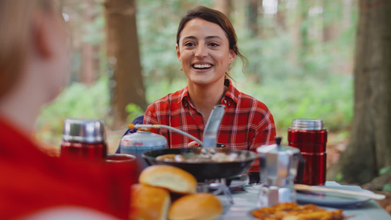 dos amigas en vacaciones de campamento en el bosque cocinando comida sentadas en una tienda juntos