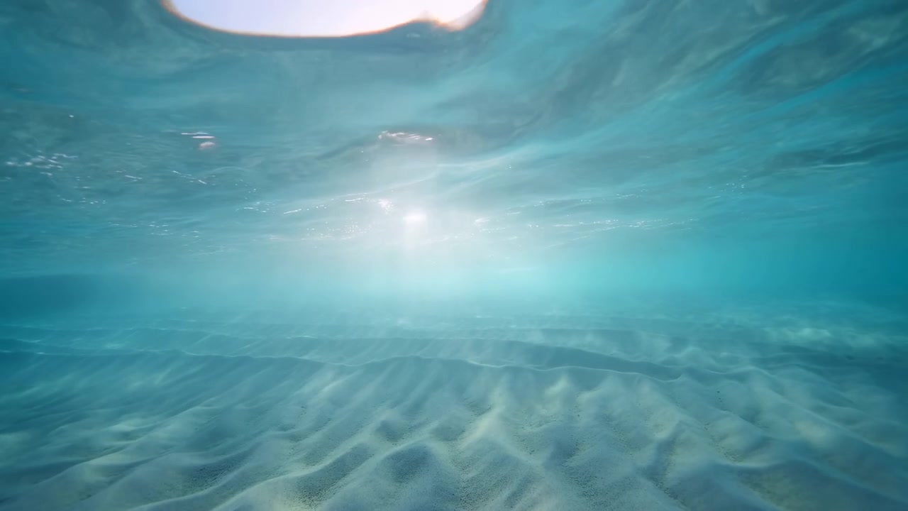 水中のターコイズ色の砂と太陽の光が、穏やかなさざ波ときらめく波、そして柔らかな光で静かな海の景色を作り出す。