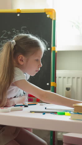 playful little boy jumps to serious sister checking homework in home classroom. toddler brother with ruler interested in lessons with girl at home