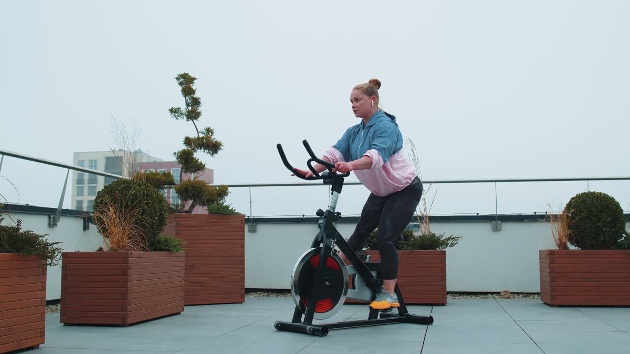 mujer blanca sana haciendo ejercicio en una máquina de ciclismo estacionaria bicicleta en el gimnasio de la azotea de la casa