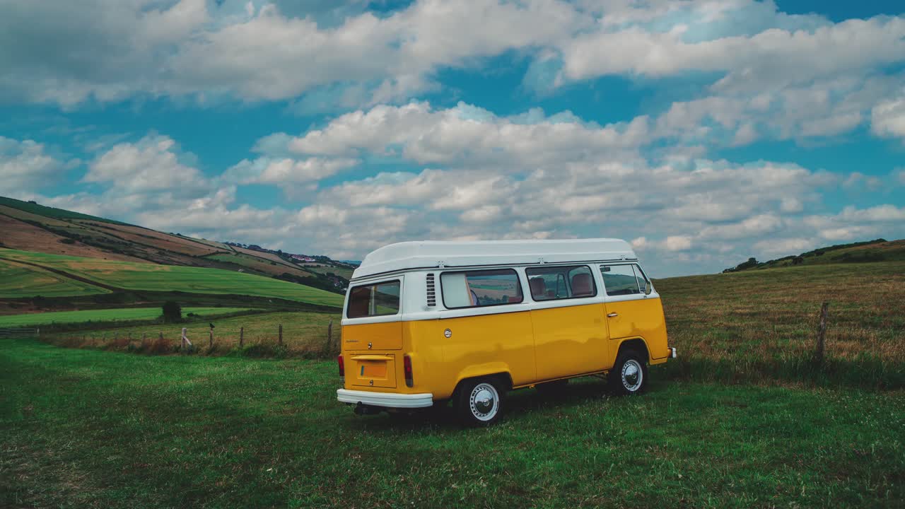 cinemagrafía de 4k uhd: bucle de video continuo de una autocaravana volkswagen vw t2 bulli clásica de pie en un campo verde en una tarde soleada en inglaterra con cielo azul, las nubes se mueven rápidamente