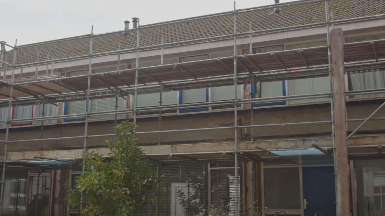 Pan of a row of houses under renovation with scaffolds put up against the facades of the homes