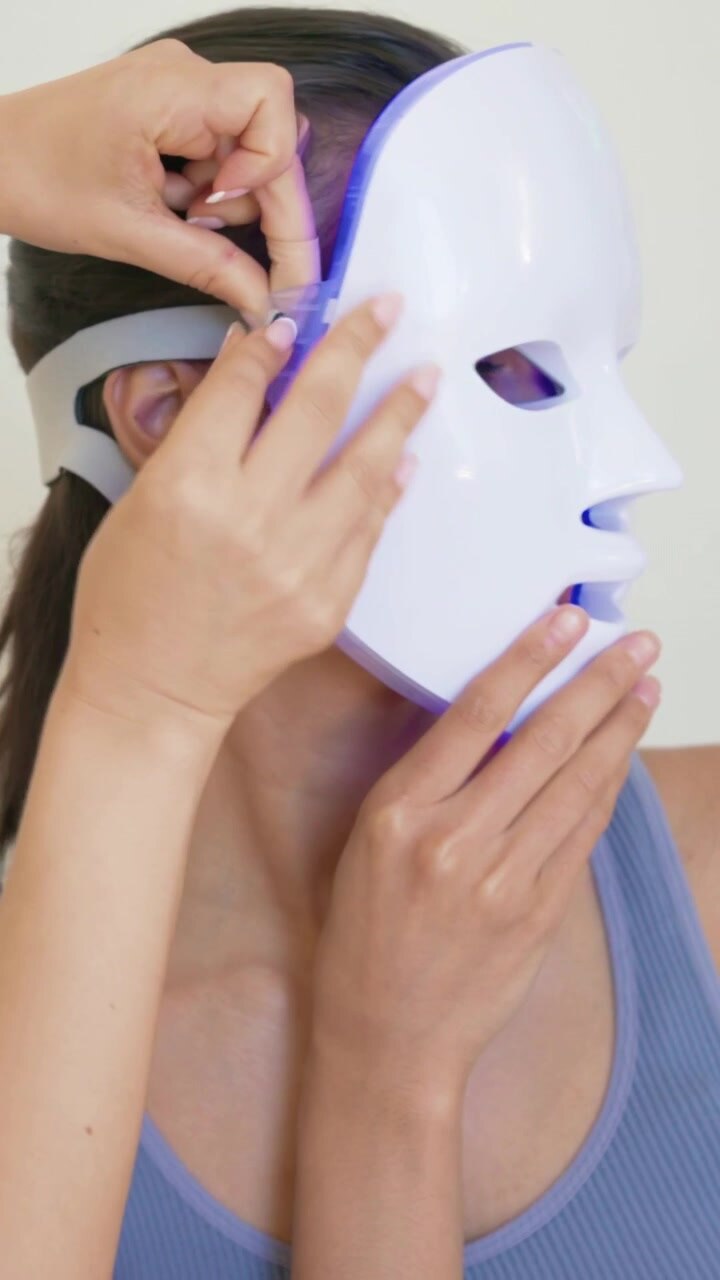 Vertical video: Leaning aid in dark top, hoops fitting LED mask for skincare securing strap bedroom