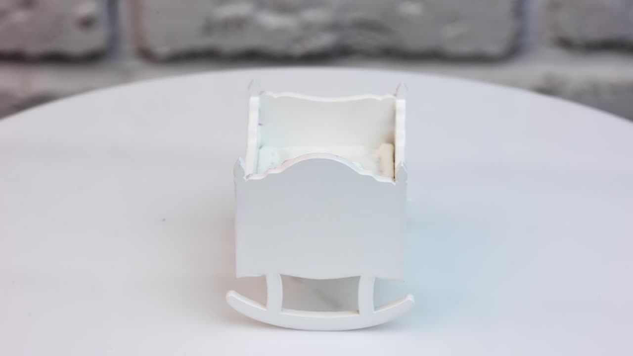 White cradle for a tiny doll at the spinning stand. A crib decorated with carved elements colored pink. Close up.