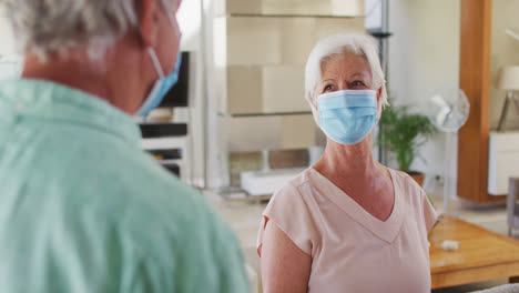 senior caucasian couple wearing face masks greeting each other by touching elbows at home