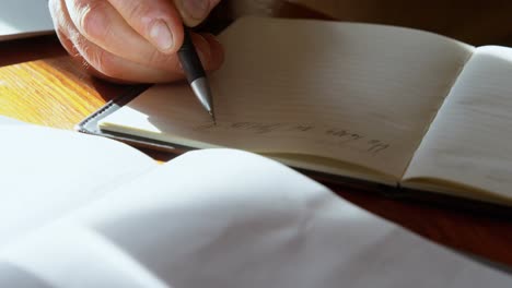 senior man writing on diary in kitchen at home 4k