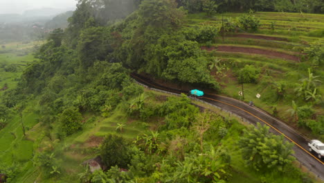 Aerial-view-of-a-truck-driving-on-the-hill-road-past-farm-fields-in-rural-countryside-in-Bali.-Car-traffic-near-rainforest-in-tropical-Asian-countryside