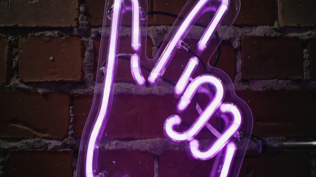 La telecamera si sposta rivelando un'insegna al neon viola a forma di mano su una parete di mattoni, per mostrare i morsetti di fissaggio e la canalina.
