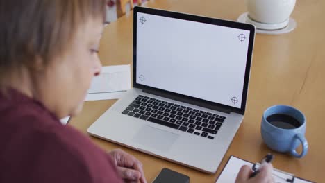 mujer mayor afroamericana en la mesa de comedor, usando una computadora portátil con espacio de copia en la pantalla y escribiendo