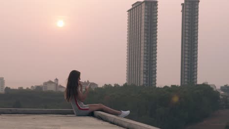 pretty-young-woman-in-grey-dress-and-sneakers-sits-on-roof