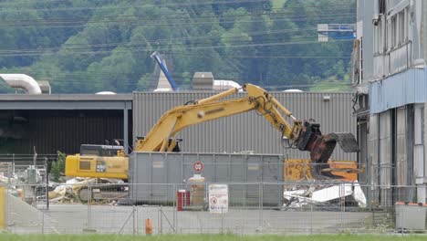 Bagger-Mit-Hydraulischer-Klaue-Zum-Abbau-Eines-Großen-Gebäudes-In-Der-Schweiz-Mit-Großem-Container-Daneben