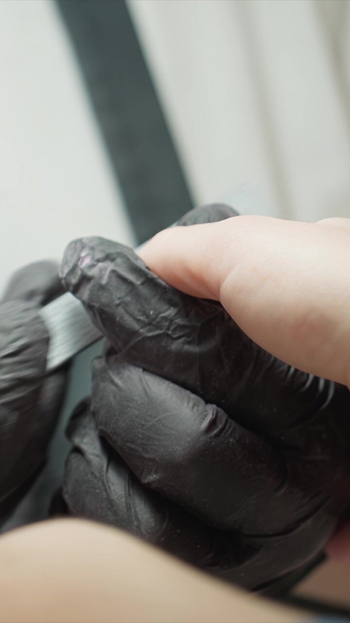 Close up shows gloved fingers carefully holding and filing toe nail. focus remains on texture of skin under bright soft lighting with minimal background detail