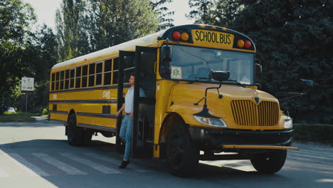 Conductor-Hombre-Saliendo-De-La-Cabina-Del-Autobús-Escolar.-Autobús-Escolar-Vacío-Parado-En-El-Estacionamiento.
