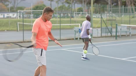 two diverse male friends playing doubles returning ball on outdoor tennis court in slow motion
