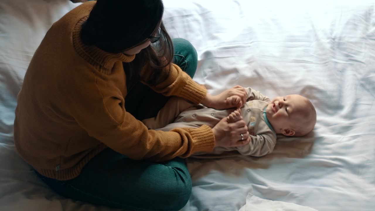 Donna che ride e gioca con il suo bambino piccolo su un letto bianco. Mamma e bambino.