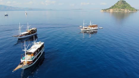 A-group-of-three-small-cruise-ships-floating-on-calm-waters-near-Pulau-Kelor-island,-close-to-Komodo-Park,-showcasing-the-tranquil-beauty-of-Indonesia-and-Asia