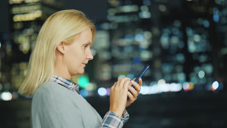 una mujer joven usa un teléfono inteligente en el fondo de las luces de la ciudad nocturna nueva york usa