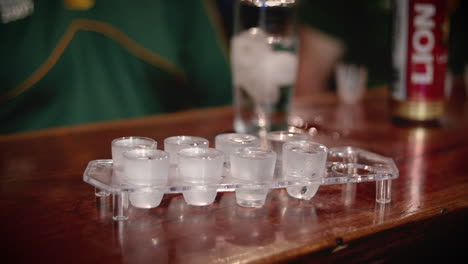 a striking image capturing a female hand with sleek black nails placing eight shots on the bar counter, setting the scene for a spirited gathering or celebration