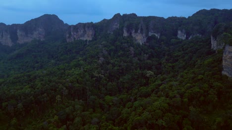 limestone cliffs and lush tropical jungle of railay beach, krabi, thailand, at dusk, creating a dramatic and serene landscape. great aerial view flight fly reverse drone