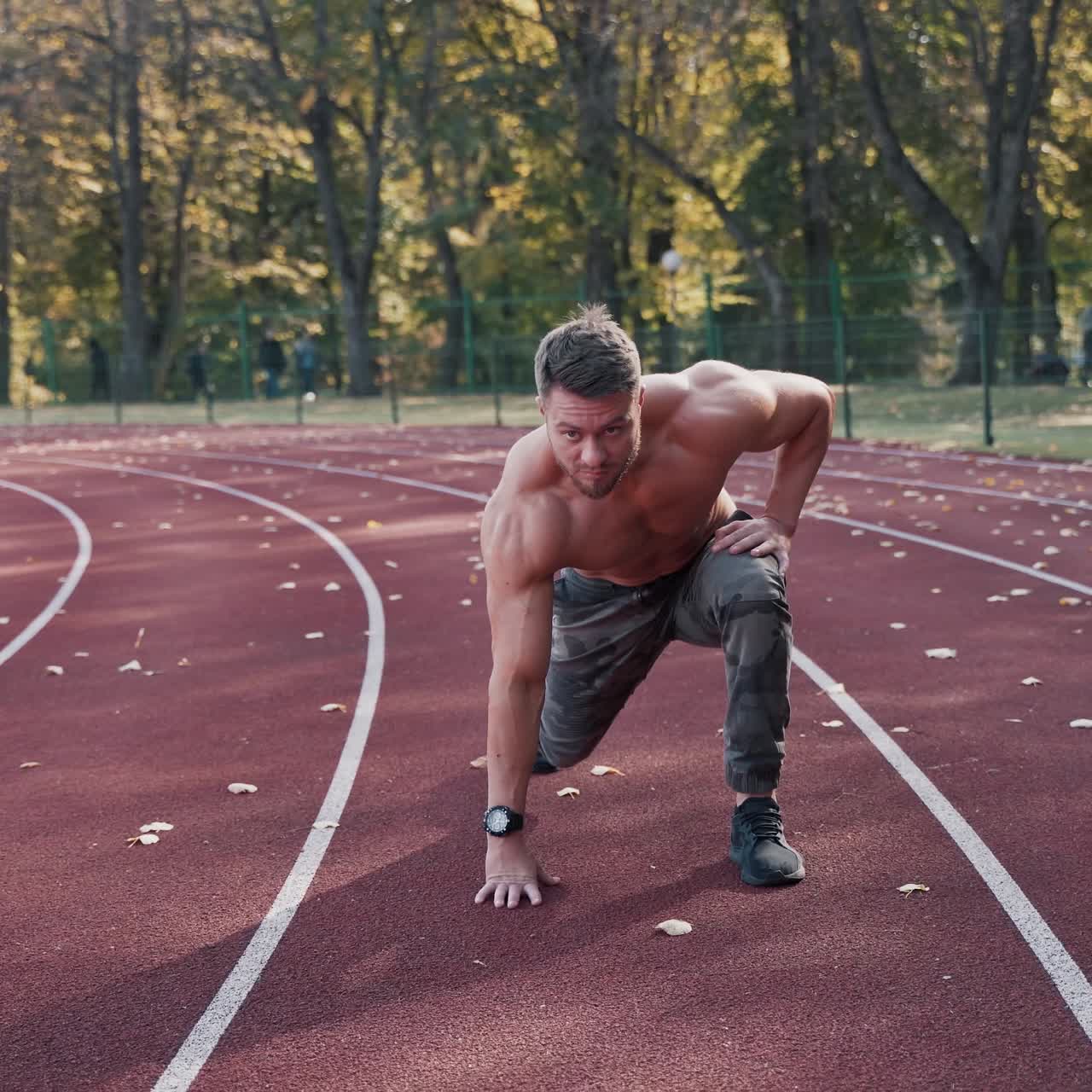 Shirtless athlete at the stadium. Strong muscular sportsman starts his running on the autumn background. Motion camera around.