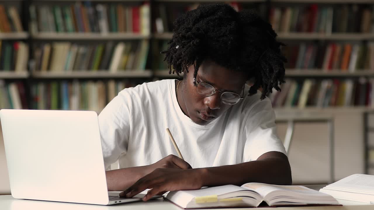 African student making notes while studying using laptop