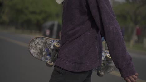 Urban-skater-walking-crossing-the-street-with-skateboard-and-violet-clothes