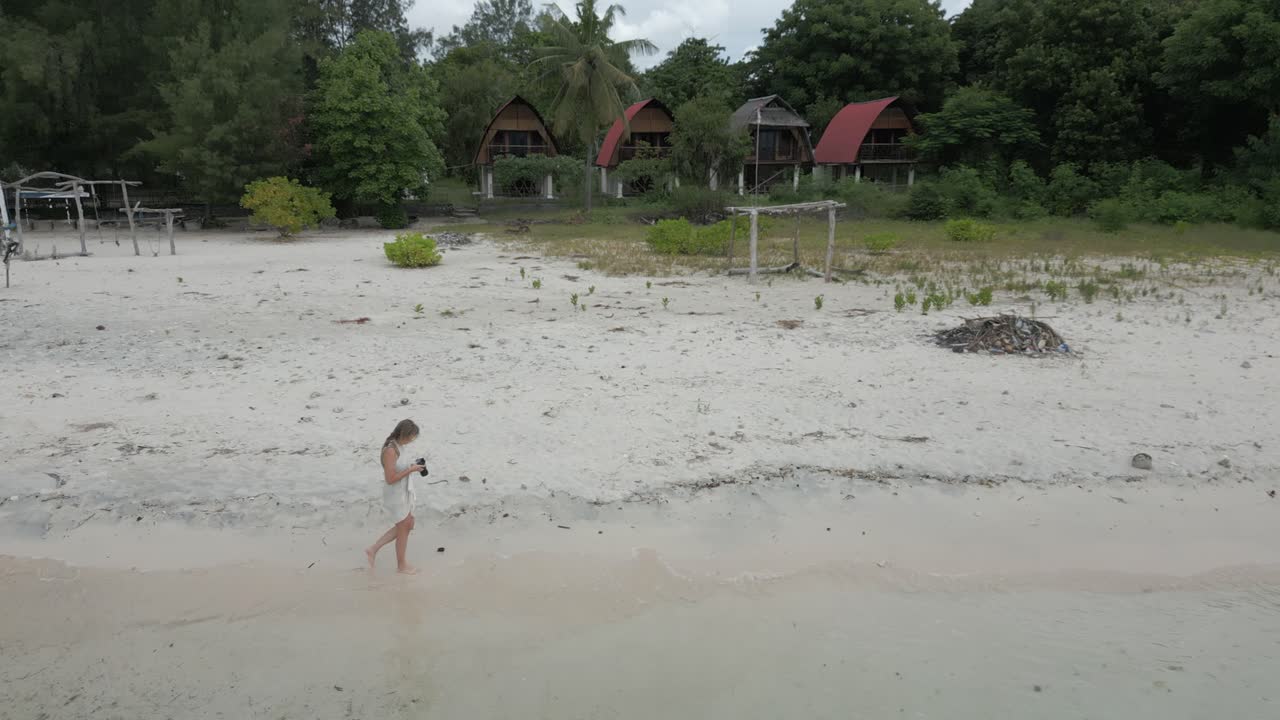 금발 백인 사진작가 여성이 모래 해변에서 외로움으로  ⁇ 고 있습니다.
