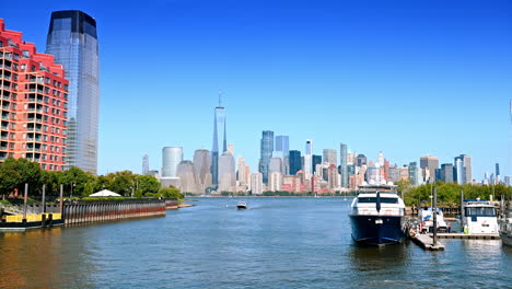 boats go by the hudson river along the pier in jersey city. skyline of modern new york downtown on sunny day at backdrop