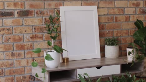 Wooden-frame-with-copy-space-on-white-background-with-plants-on-desk-against-brick-wall