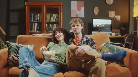 joyful girlfriend and boyfriend eating popcorn and watching tv in living room