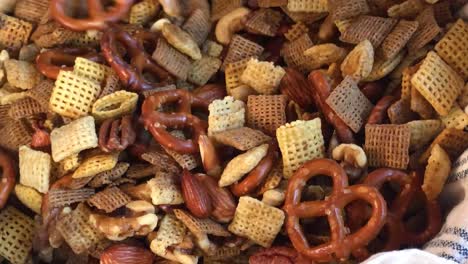 stirring holiday party mix of nuts, grain cereals, and pretzels in large bowl flat lay